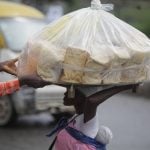 A man who is wanting to buy bread is helping a vendor drop a load of loaves off her head as Muslim faithful are praying to mark the Eid-El-Kabir festival in Ikeja, Lagos, Nigeria, on Sunday, June 16, 2024.