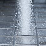 White fertilizer pellets fall through the metal bars of a screen designed to break up chunks.