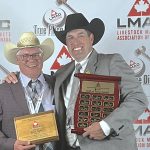 Two men wearing suits and cowboy hats, one black and one white, pose for a photo, smiling, while holding a plaque.