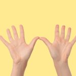 Two hands lifted up, palms towards camera, against a yellow background.