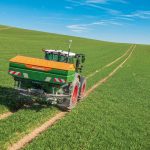 A new Amazone spreader drives along the ruts in a field.