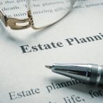 A pen and a pair of glasses sit on top of a piece of paper with "Estate Planning" written on it.