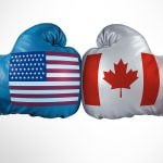 A photo illustration showing two boxing gloves touching, as boxers do at the beginning of a fight, with one glove having a U.S. flag on it and the other a Canadian flag.