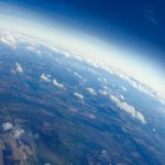The curvature of the Earth and the "checker board" appearance of various crops, as well as some clouds, are visible in this aerial photo.