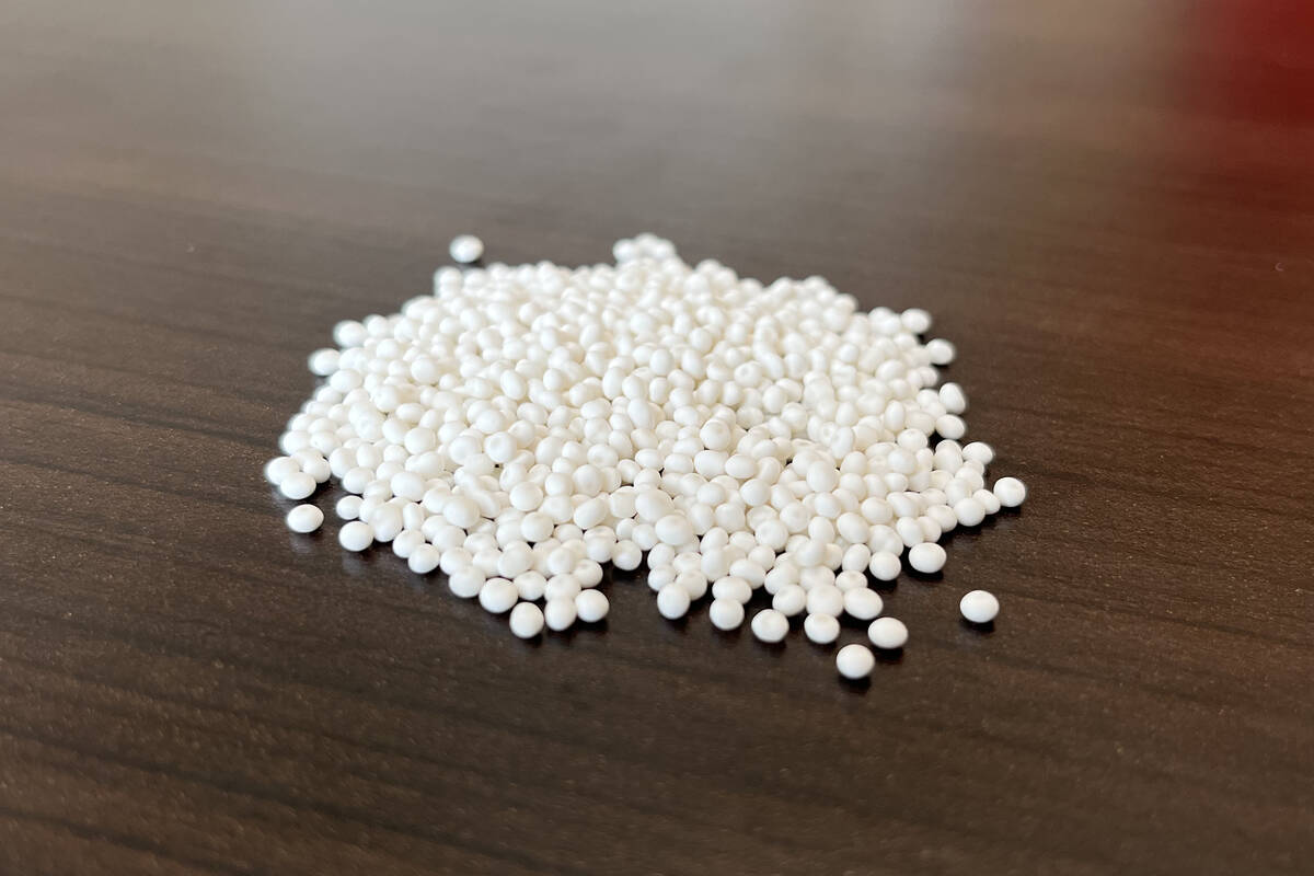 White granules of fertilizer in a small pile on a dark surface.