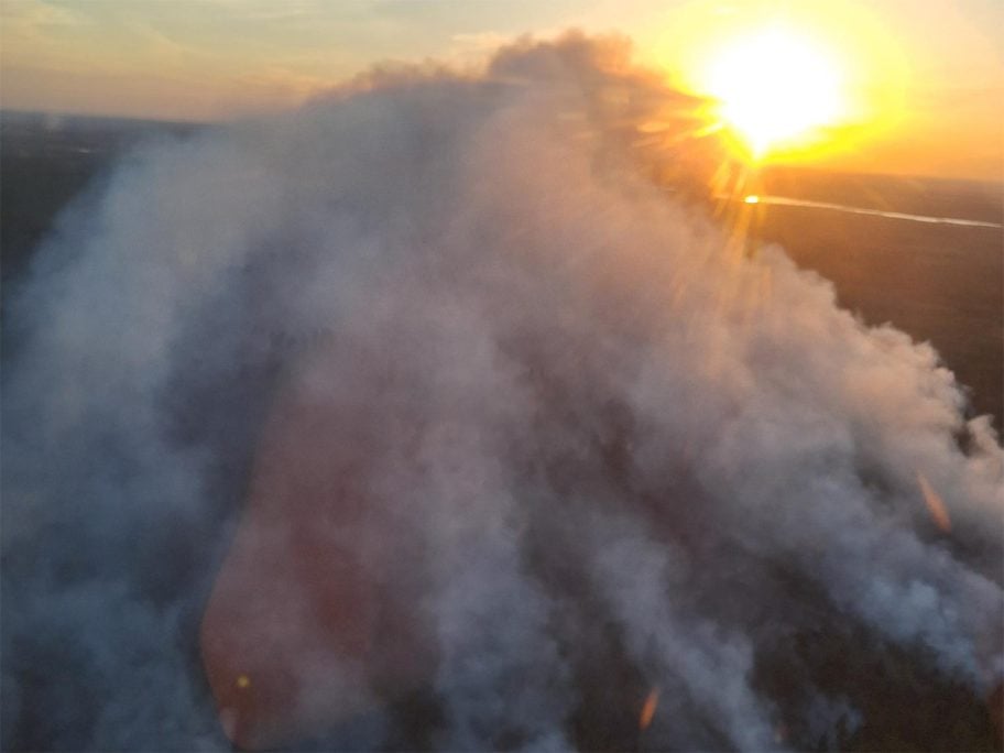 An aerial view of the Lobstick fire near Shellbrook, Saskatchewan, as smoke rises from the forest below and the sun sets in the west.