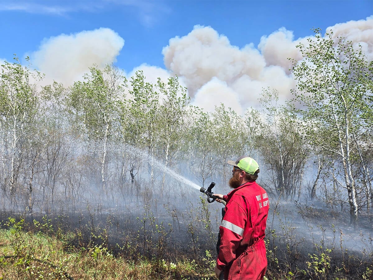 A fireman in red coveralls uses a hose to put water onto the Lobstick fire near Duck Lake, Saskatchewan. Photo from Duck Lake Fire Department's Facebook page.