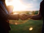 Close up of businesswoman and farm owner shaking hands in the field at sunset.