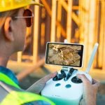 Female Unmanned Aircraft System (UAV) Quadcopter Drone Pilot with Controller Inspecting New House Framing. Photo: Getty Images